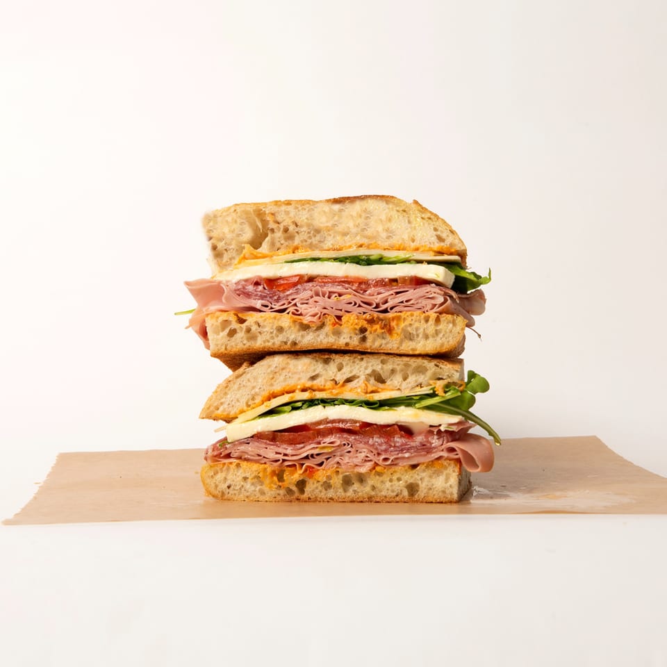 A Deliche sandwich, cut in half and stacked, revealing layers of meat, cheese, and greens.