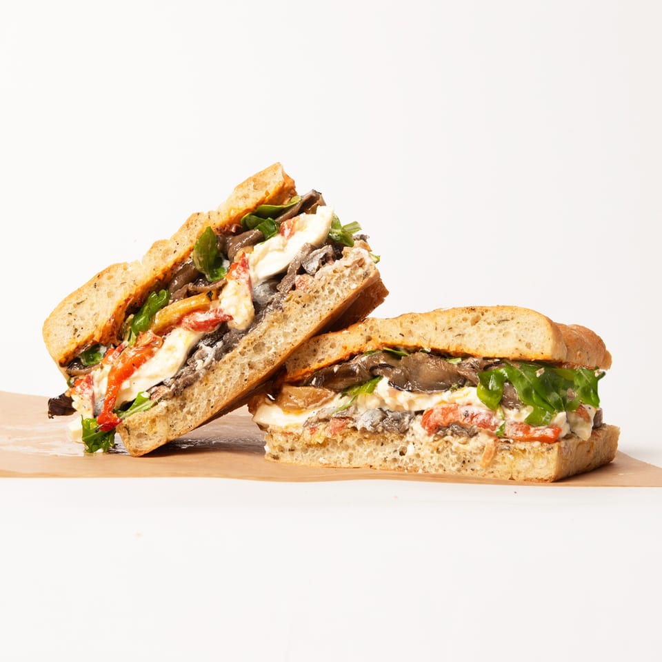Two halves of a Deliche sandwich, filled with mushrooms, cheese, roasted red peppers, and greens.