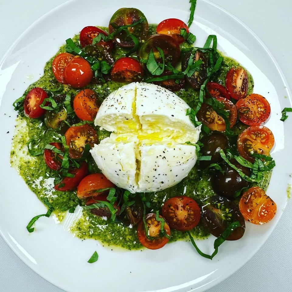 Burrata cheese with pesto, halved cherry tomatoes, and fresh basil on a white plate.