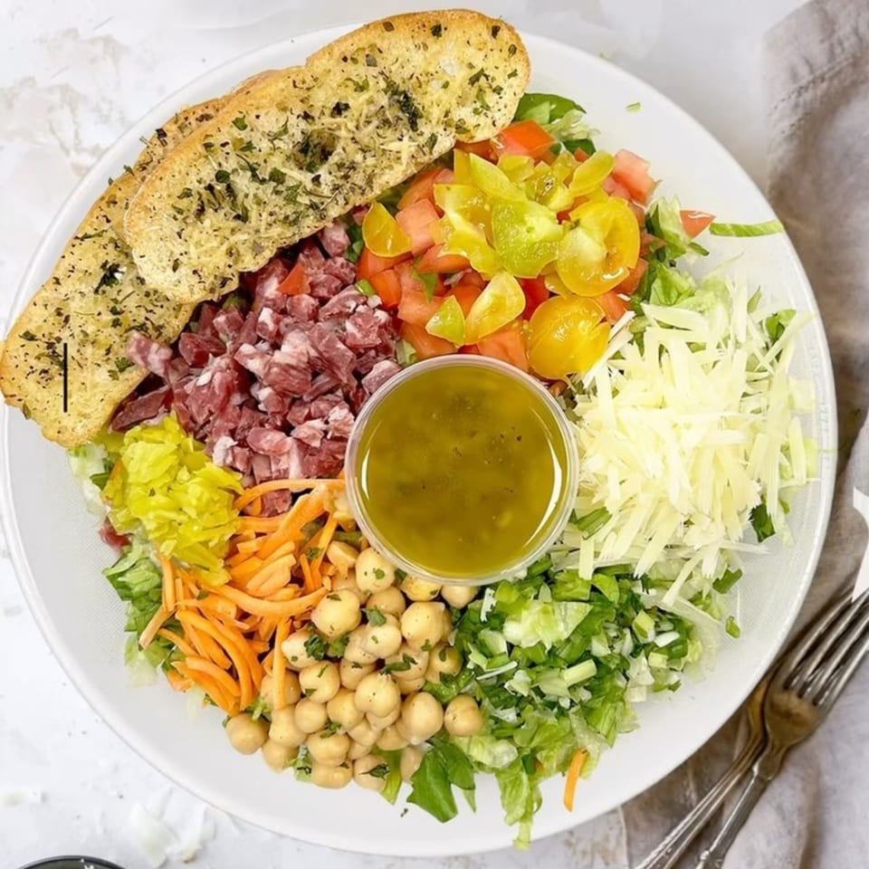 A vibrant Deliche salad with salami, chickpeas, tomatoes, cheese, and garlic bread.
