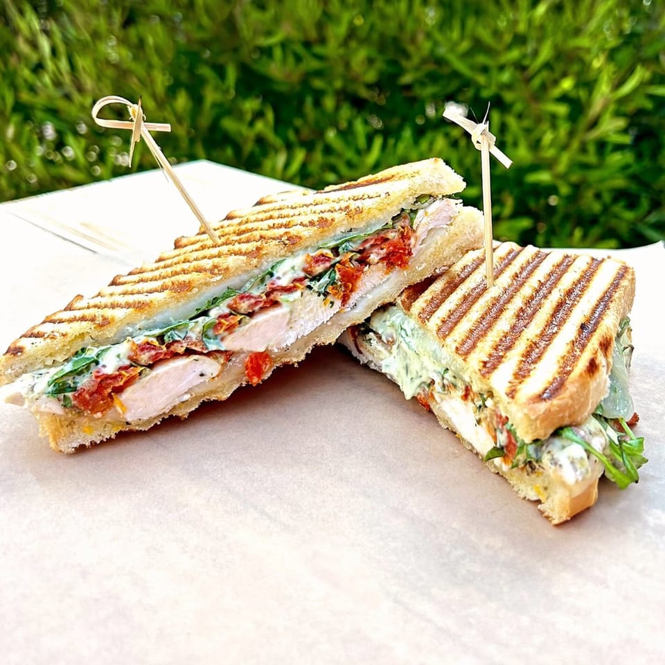 Two halves of a grilled chicken panini with sun-dried tomatoes, arugula, and creamy sauce.