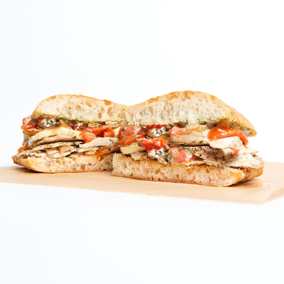 Deliche chicken sandwich with roasted red peppers and creamy sauce on ciabatta bread, cut in half.
